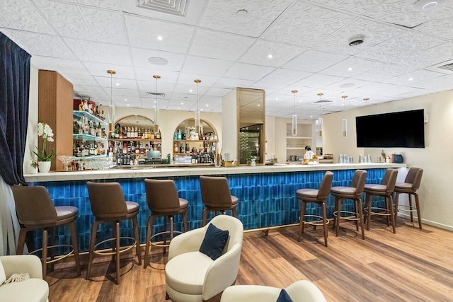 bar with decorative light fixtures, visible vents, a community bar, wood finished floors, and a drop ceiling