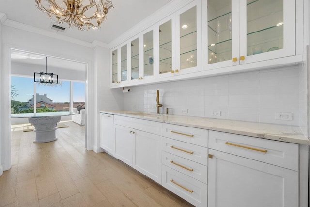 bar with hanging light fixtures, decorative backsplash, an inviting chandelier, ornamental molding, and a sink