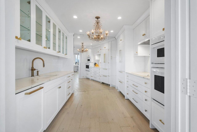 kitchen featuring a notable chandelier, hanging light fixtures, glass insert cabinets, white cabinetry, and light stone countertops