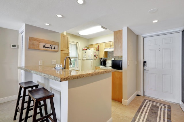 kitchen featuring backsplash, a kitchen breakfast bar, white refrigerator, light brown cabinetry, and kitchen peninsula