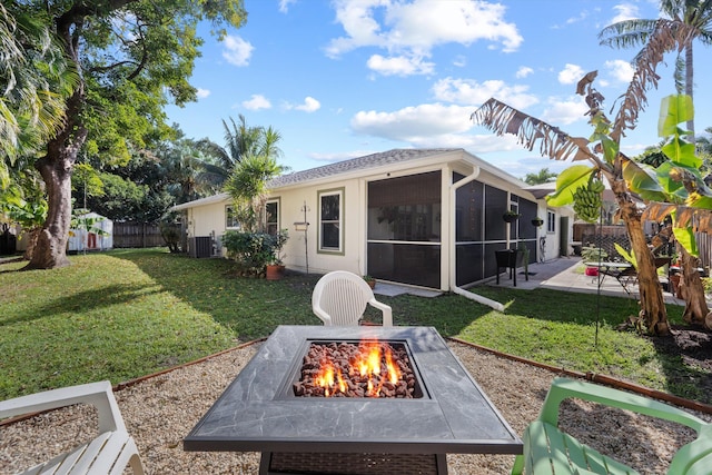 rear view of house with a patio, a lawn, a fire pit, central air condition unit, and a sunroom