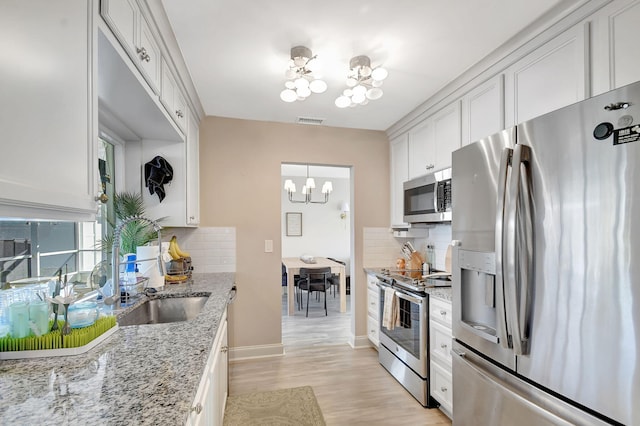 kitchen with sink, light stone counters, appliances with stainless steel finishes, a notable chandelier, and white cabinets