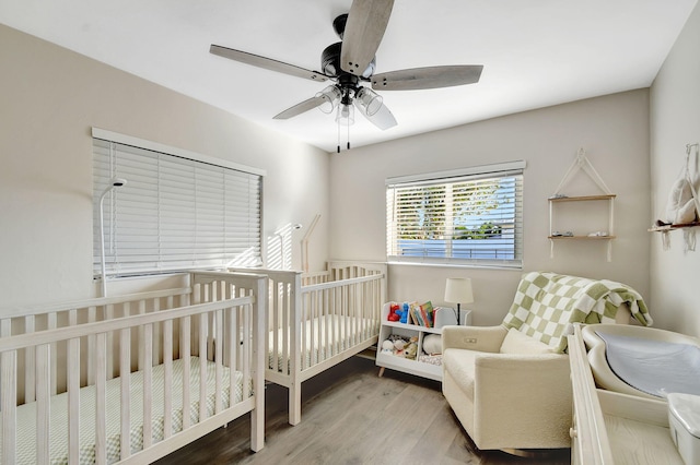 bedroom featuring a nursery area, ceiling fan, and light wood-type flooring