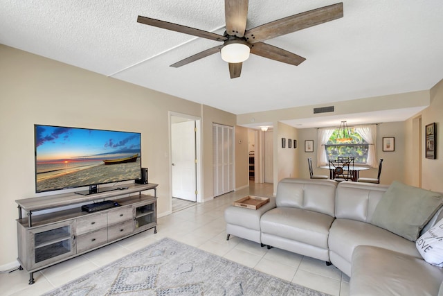 living room featuring visible vents, light tile patterned flooring, ceiling fan, a textured ceiling, and baseboards