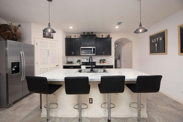 kitchen with stainless steel appliances, decorative light fixtures, and a kitchen island with sink