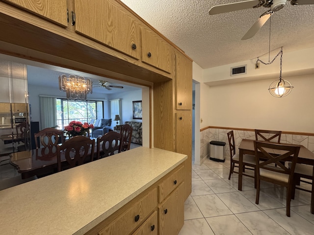 kitchen featuring ceiling fan with notable chandelier, hanging light fixtures, and a textured ceiling