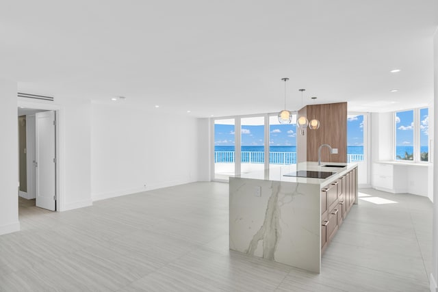 kitchen with sink, a water view, light stone countertops, an island with sink, and decorative light fixtures