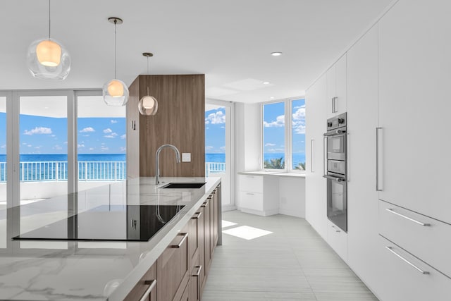 kitchen with white cabinetry, sink, hanging light fixtures, black electric stovetop, and a water view