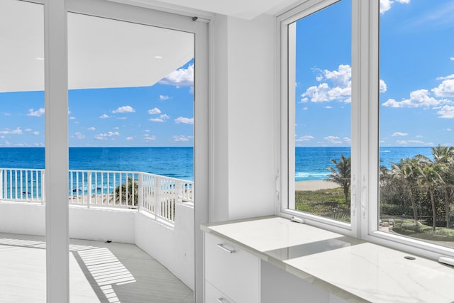 interior space featuring a balcony, a water view, and a view of the beach