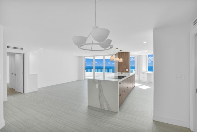 kitchen featuring a wall of windows, a spacious island, a water view, light stone counters, and decorative light fixtures