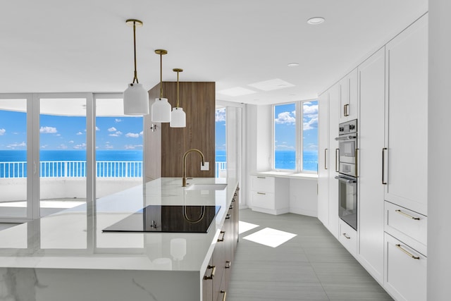 kitchen with sink, a water view, an island with sink, black electric cooktop, and decorative light fixtures