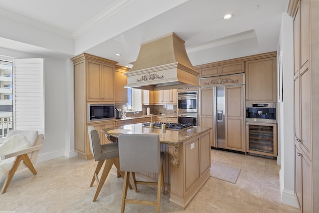 kitchen with a breakfast bar area, custom exhaust hood, light stone counters, built in appliances, and a center island