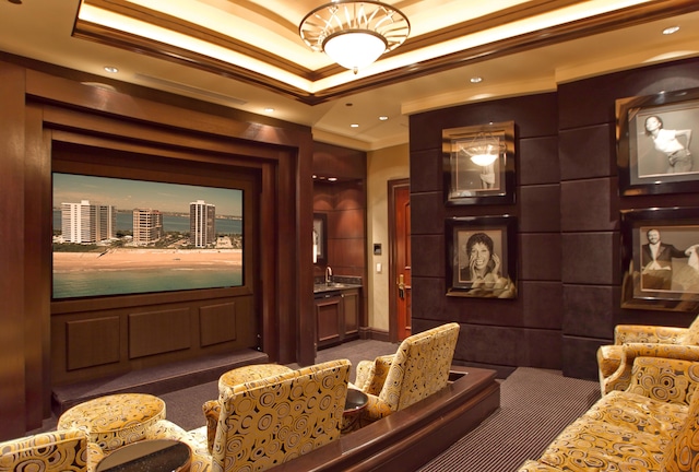 home theater room with dark colored carpet, ornamental molding, and a tray ceiling