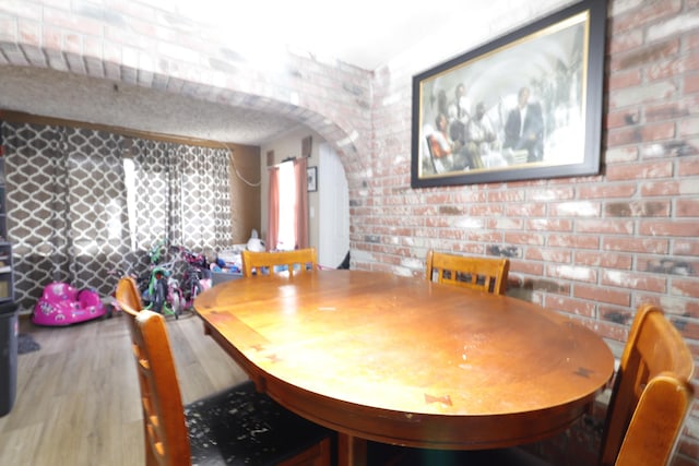 dining space featuring wood-type flooring and brick wall