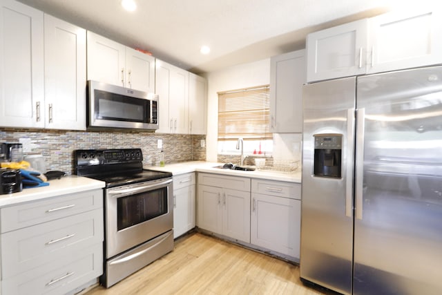 kitchen with sink, appliances with stainless steel finishes, white cabinetry, light hardwood / wood-style floors, and decorative backsplash