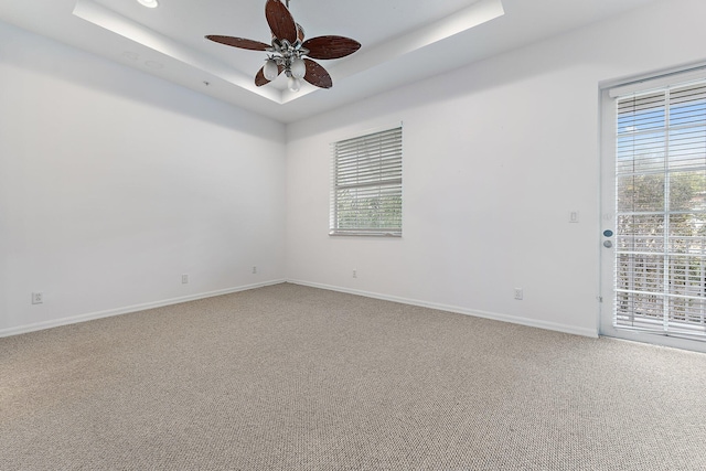 carpeted spare room with a tray ceiling, a wealth of natural light, and ceiling fan