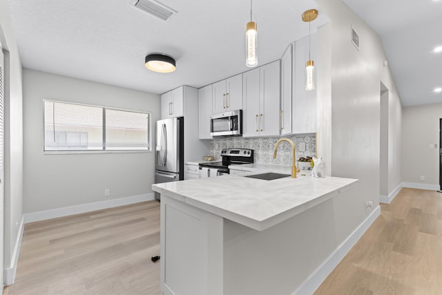 kitchen featuring sink, hanging light fixtures, white cabinets, stainless steel appliances, and backsplash