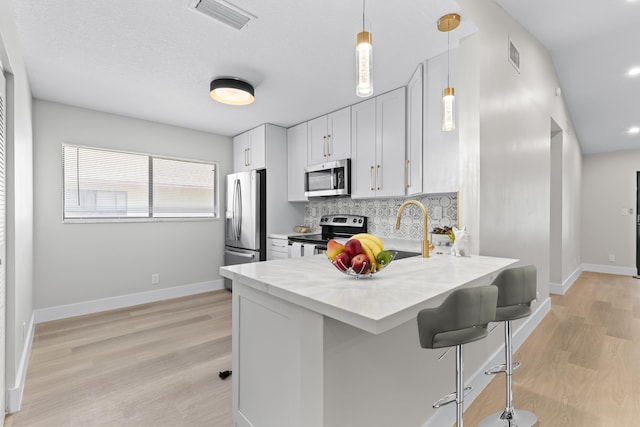 kitchen featuring pendant lighting, white cabinetry, backsplash, stainless steel appliances, and light hardwood / wood-style flooring