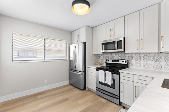 kitchen featuring white cabinets, backsplash, light stone counters, light hardwood / wood-style floors, and stainless steel appliances