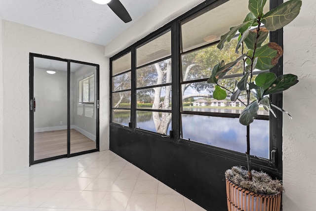 doorway featuring a water view, light tile patterned floors, a textured ceiling, and ceiling fan