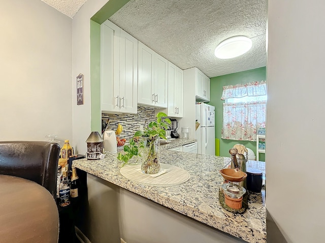 kitchen featuring white cabinetry, a textured ceiling, light stone counters, and decorative backsplash