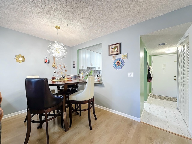 dining room with a notable chandelier, light hardwood / wood-style flooring, and a textured ceiling