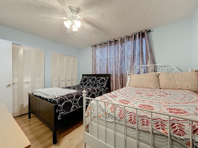 bedroom featuring hardwood / wood-style flooring, ceiling fan, two closets, and a textured ceiling