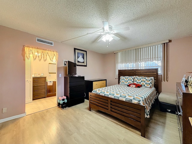 bedroom with ceiling fan, ensuite bath, light hardwood / wood-style floors, and a textured ceiling