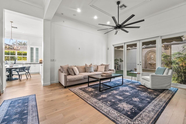 living room with a towering ceiling, ceiling fan with notable chandelier, crown molding, light wood-type flooring, and french doors