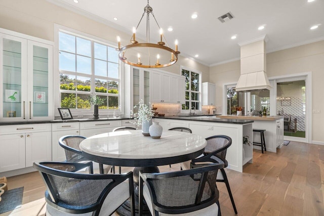 dining area featuring an inviting chandelier, sink, crown molding, and light hardwood / wood-style flooring