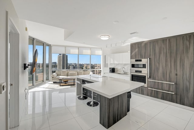 kitchen featuring a breakfast bar, tasteful backsplash, a kitchen island, stainless steel double oven, and white cabinets