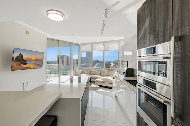 kitchen with light tile patterned floors, a wall of windows, double oven, dark brown cabinets, and track lighting