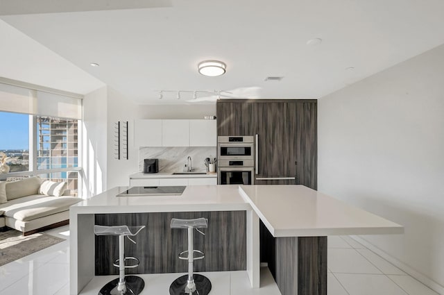 kitchen with stainless steel double oven, sink, a center island, and white cabinets