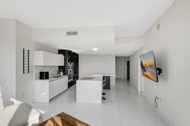 kitchen featuring sink, white cabinetry, light tile patterned floors, a kitchen breakfast bar, and a kitchen island