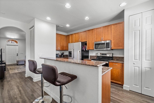 kitchen featuring a breakfast bar, dark stone counters, dark hardwood / wood-style floors, a kitchen island, and stainless steel appliances