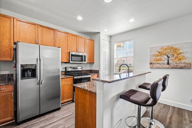 kitchen with a kitchen bar, sink, dark stone countertops, stainless steel appliances, and hardwood / wood-style floors