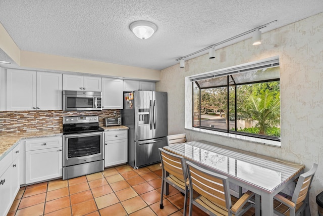 kitchen with decorative backsplash, light stone countertops, white cabinets, and appliances with stainless steel finishes