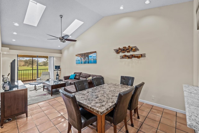 tiled dining space with ceiling fan, a skylight, and high vaulted ceiling