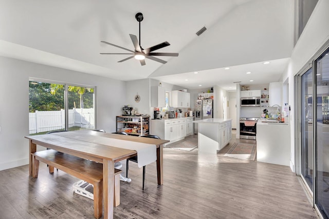 dining area with sink, high vaulted ceiling, ceiling fan, and light wood-type flooring