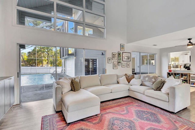 living room featuring a high ceiling, ceiling fan, and light wood-type flooring