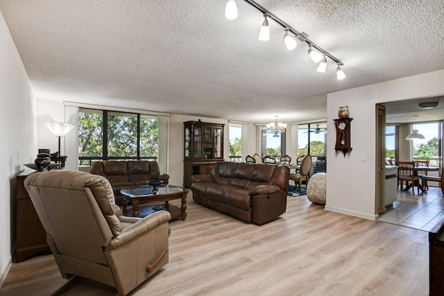 living room with rail lighting, a chandelier, a textured ceiling, and light wood-type flooring