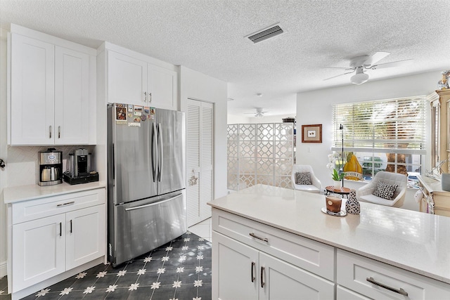 kitchen with ceiling fan, stainless steel fridge, a textured ceiling, and white cabinets