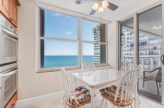 dining space with ceiling fan, plenty of natural light, a textured ceiling, and a water view