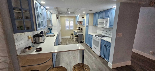 kitchen featuring blue cabinets, wood-type flooring, sink, kitchen peninsula, and white appliances