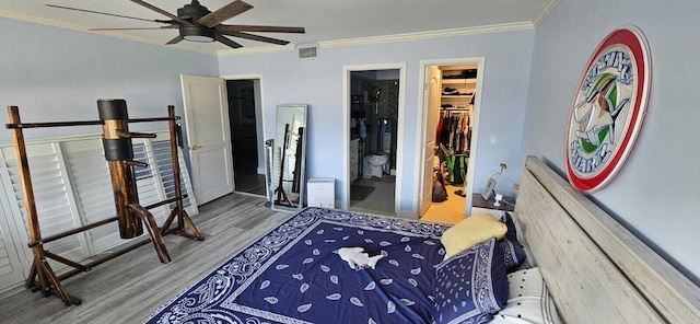 bedroom with connected bathroom, crown molding, a walk in closet, wood-type flooring, and a closet