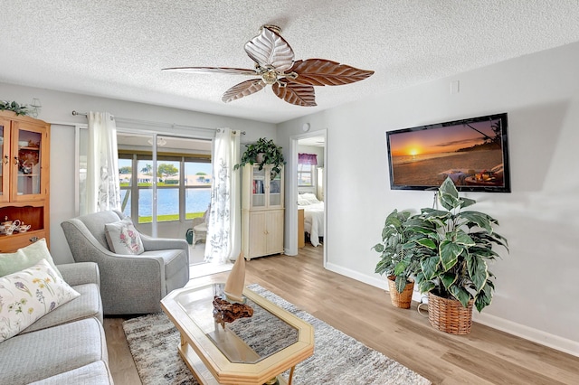 living room with ceiling fan, a textured ceiling, and light wood-type flooring