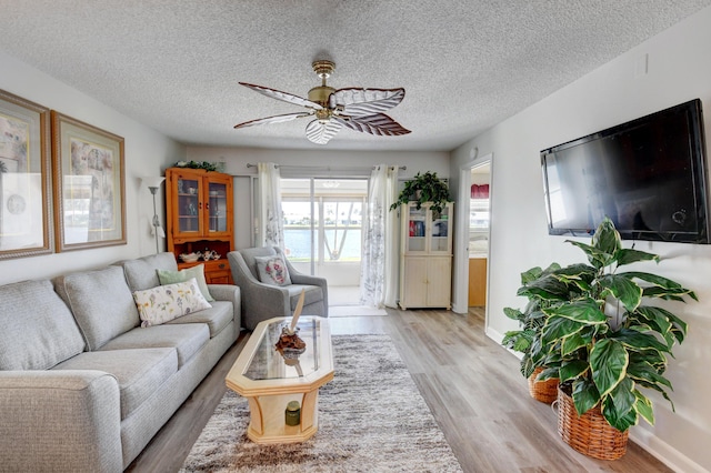 living room featuring ceiling fan, light hardwood / wood-style flooring, and a textured ceiling