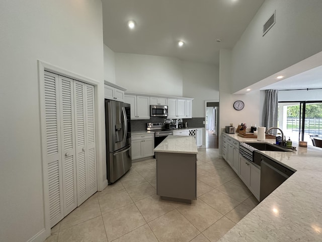 kitchen with sink, a kitchen island, stainless steel appliances, light stone countertops, and a high ceiling