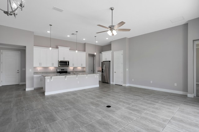 kitchen with appliances with stainless steel finishes, pendant lighting, white cabinetry, a kitchen island with sink, and ceiling fan