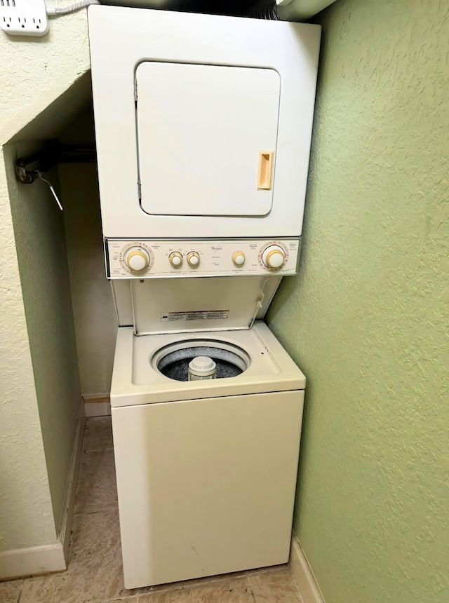 laundry room featuring laundry area, baseboards, a textured wall, and stacked washing maching and dryer